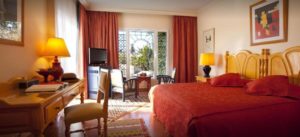 Villa Mandarine Rabat, Morocco hotel room. Cream walls, light wood desk and headboard, and burgundy curtains and bedspread