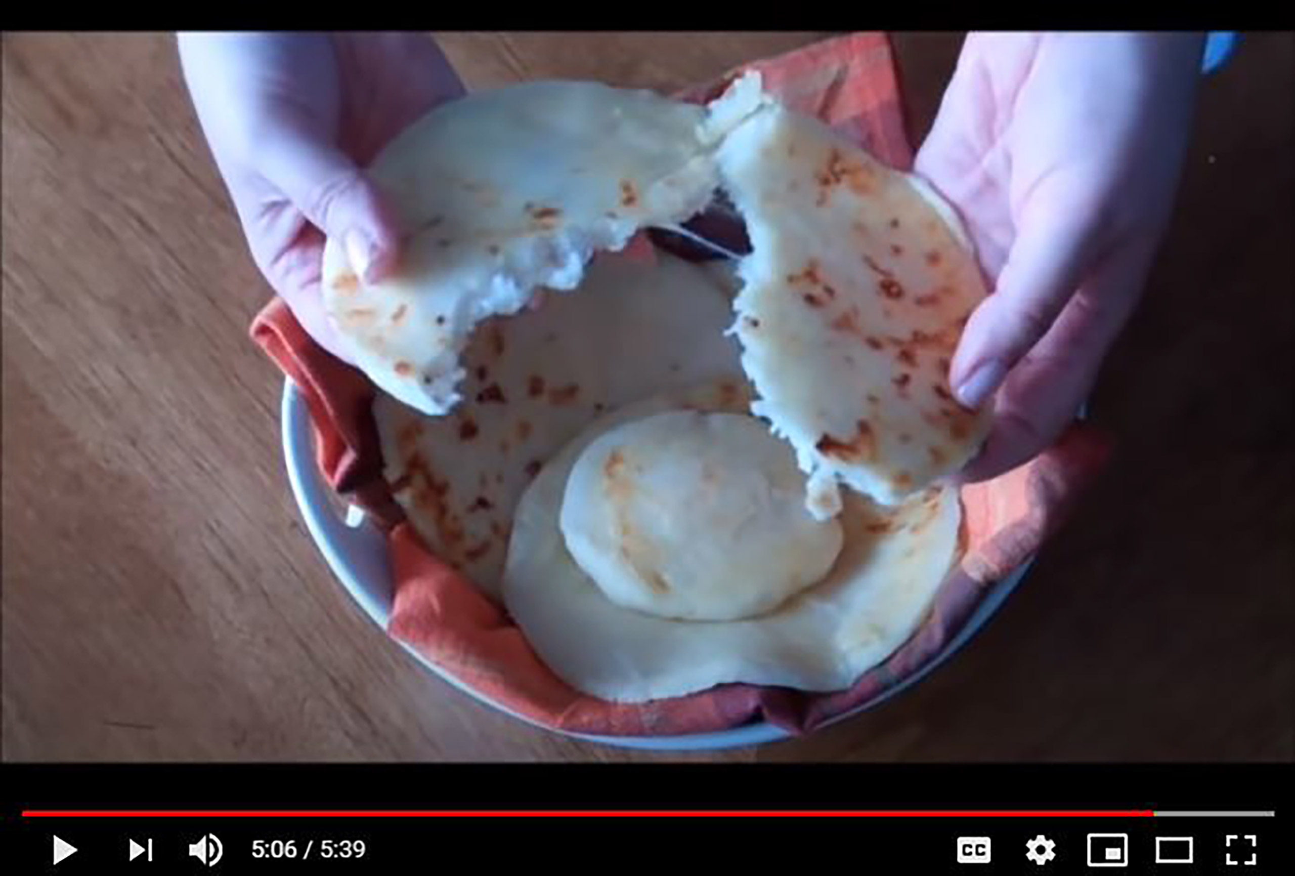 Video still of a flat, round, unleavened piece of dough called arepa being pulled apart to show the mozzarella on the inside